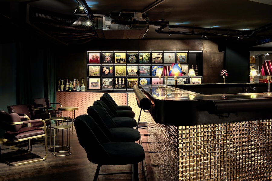 Intérieur du Sape Bar du 25hours Hotel Terminus Nord à Paris, avec comptoir lumineux, fauteuils et pochettes de vinyles exposées.